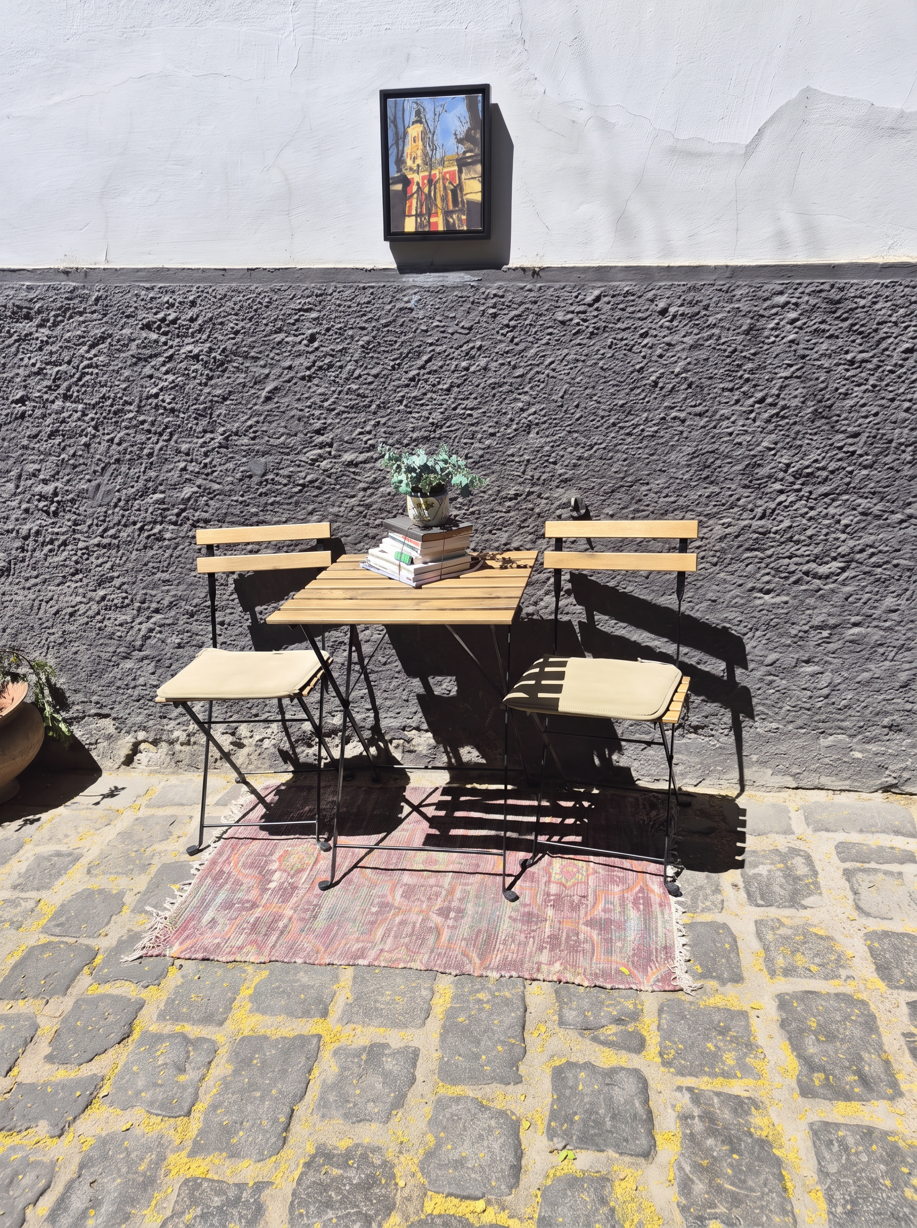 A sunny cafe table and two chairs against a textured stone wall in Szentendre, Hungary