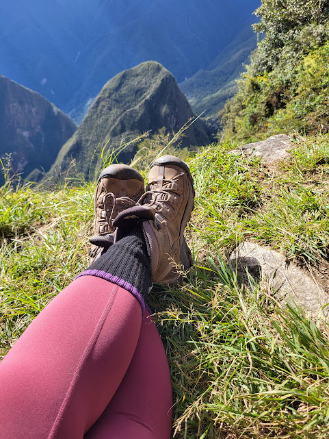 Hiking boots resting on a grassy mountain ridge overlooking a dramatic peak in Peru